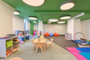 Interior Children's play room, ceiling painted green, childrens tables, play mats, toy cubbies, map of the world painted on the walls, childrens trampoline, toy kitchen, childrens lounge chairs.