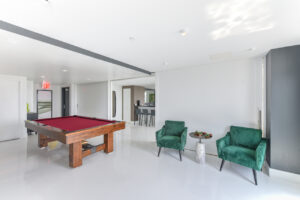 Interior Community Room, white and gray walls, red pool table, green lounge chairs, white floors, contemporary art on the walls, bar area in other room.