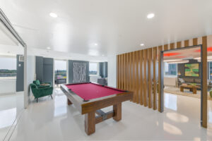 Interior Community Room, Modern art on walls, white floor, lounge area in other room, red pool table in center of room, green lounge chairs in other room.