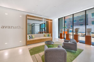Interior lobby, avanath signage, green contemporary rug, 2 lounge chairs, modern vases on pedestals in the window, built in sofa to the right of avanath signage, black round coffee table.