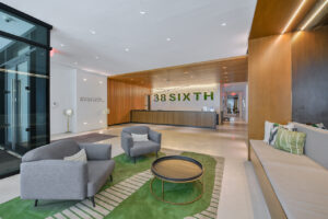 Interior Lobby, green contemporary rug, 2 lounge chairs, black coffee table, modern front desk, built in couch, avanath signage at entrance.