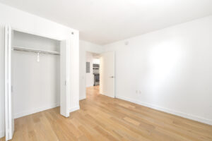 Interior Unit Bedroom, accordion closet doors, white walls, wood floors.