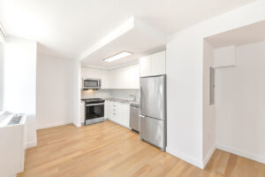 Interior Unit Kitchen, stainless steel appliances, white cabinets, wood floors, white walls.