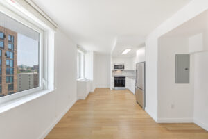 Interior Unit Kitchen, white walls wood floors, stainless steel appliances, windows with view of the city, white cabinets.